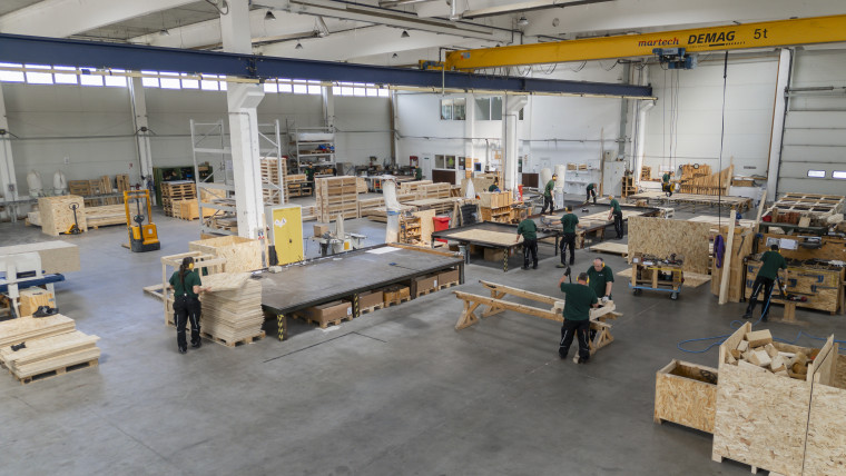 Fabrikszene mit Arbeitern, die an der Fertigung von Holzverpackungen beschäftigt sind.
