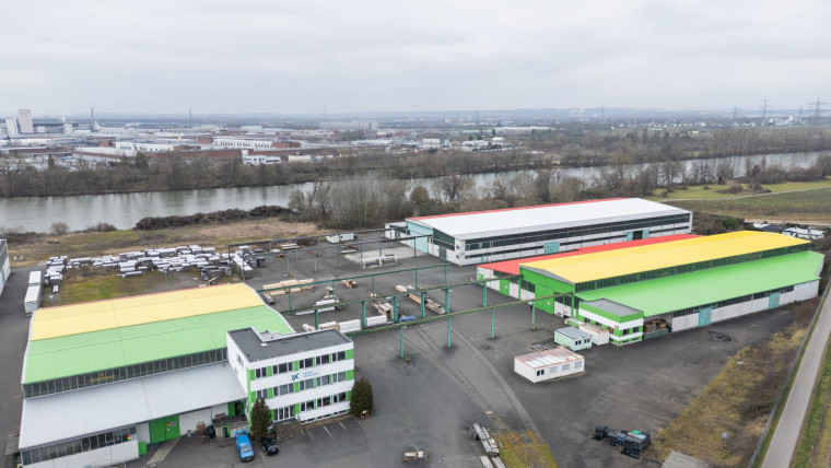 Luftaufnahme von dem Betriebsgelände von AXXUM Packaging Main-Neckar mit mehreren großen Lagerhallen und einem Fluss im Hintergrund